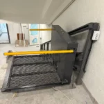 Інвалідний підйомник похилого типу з металевою платформою та жовтими поручнями, встановлений на сходах усередині будівлі