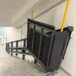 Інвалідний підйомник похилого типу з платформою та захисними бортами, встановлений уздовж сходів усередині будівлі